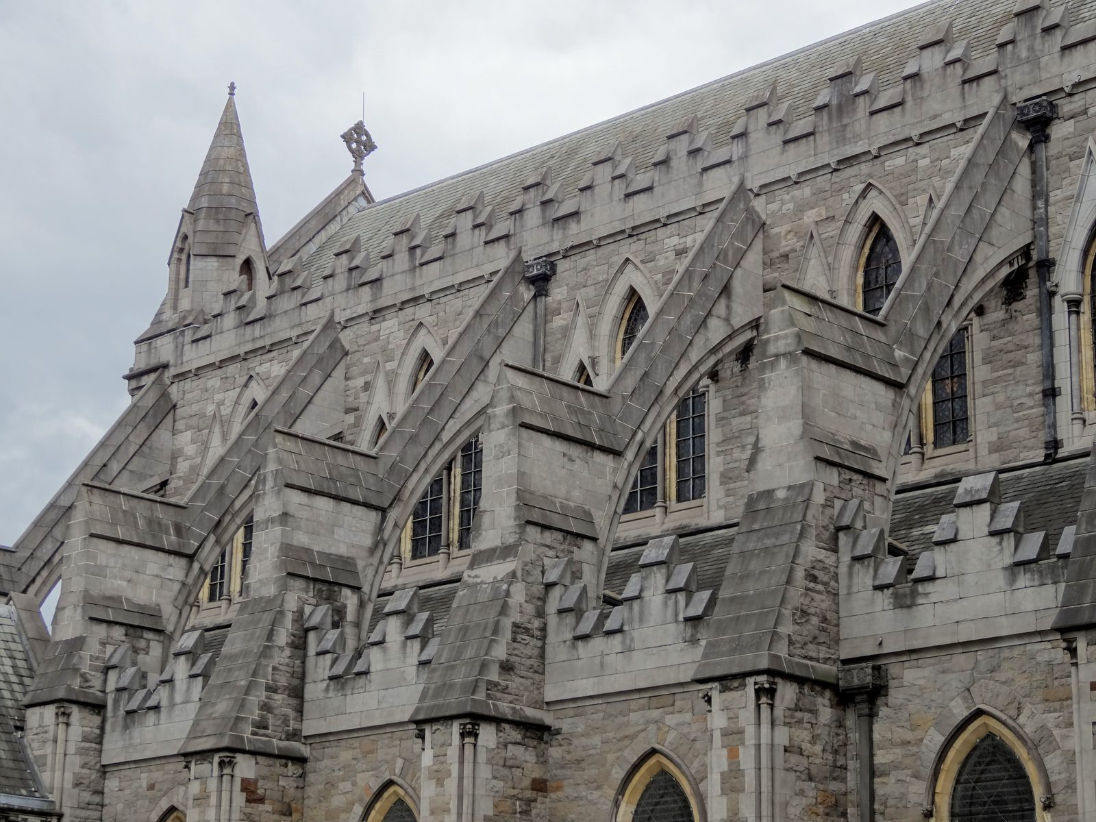 The grey stone flank of a Gothic cathedral with flying buttresses and pointed windows.