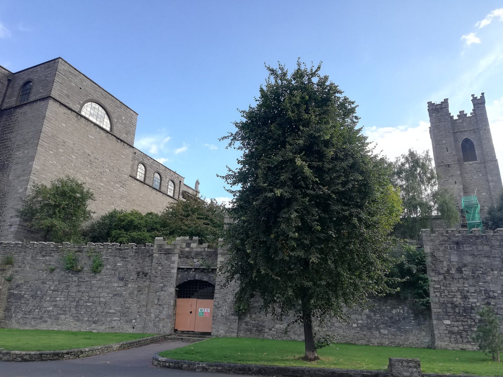 A stretch of rubble stone wall with a gateway, a church tower behind it.