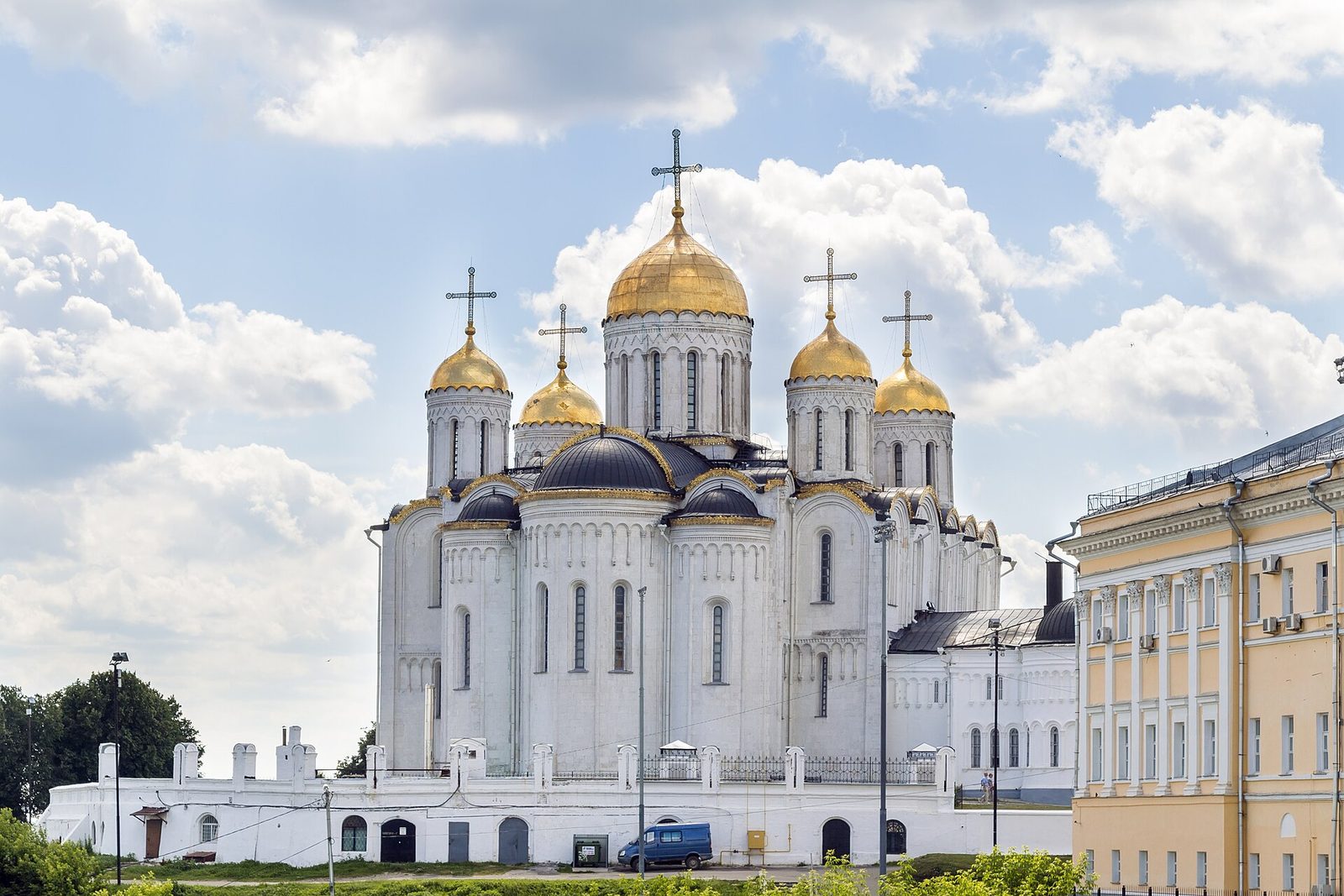 A white stone cathedral with five gilded domes under a sky of clouds.