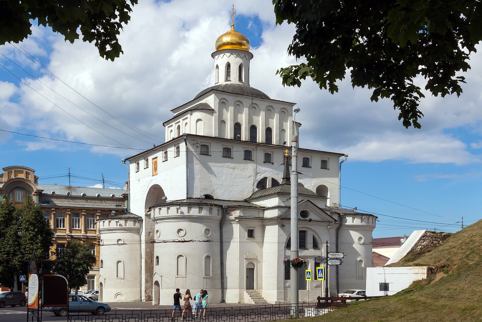A massive white stone gateway with a gilded dome on top, beside a street.