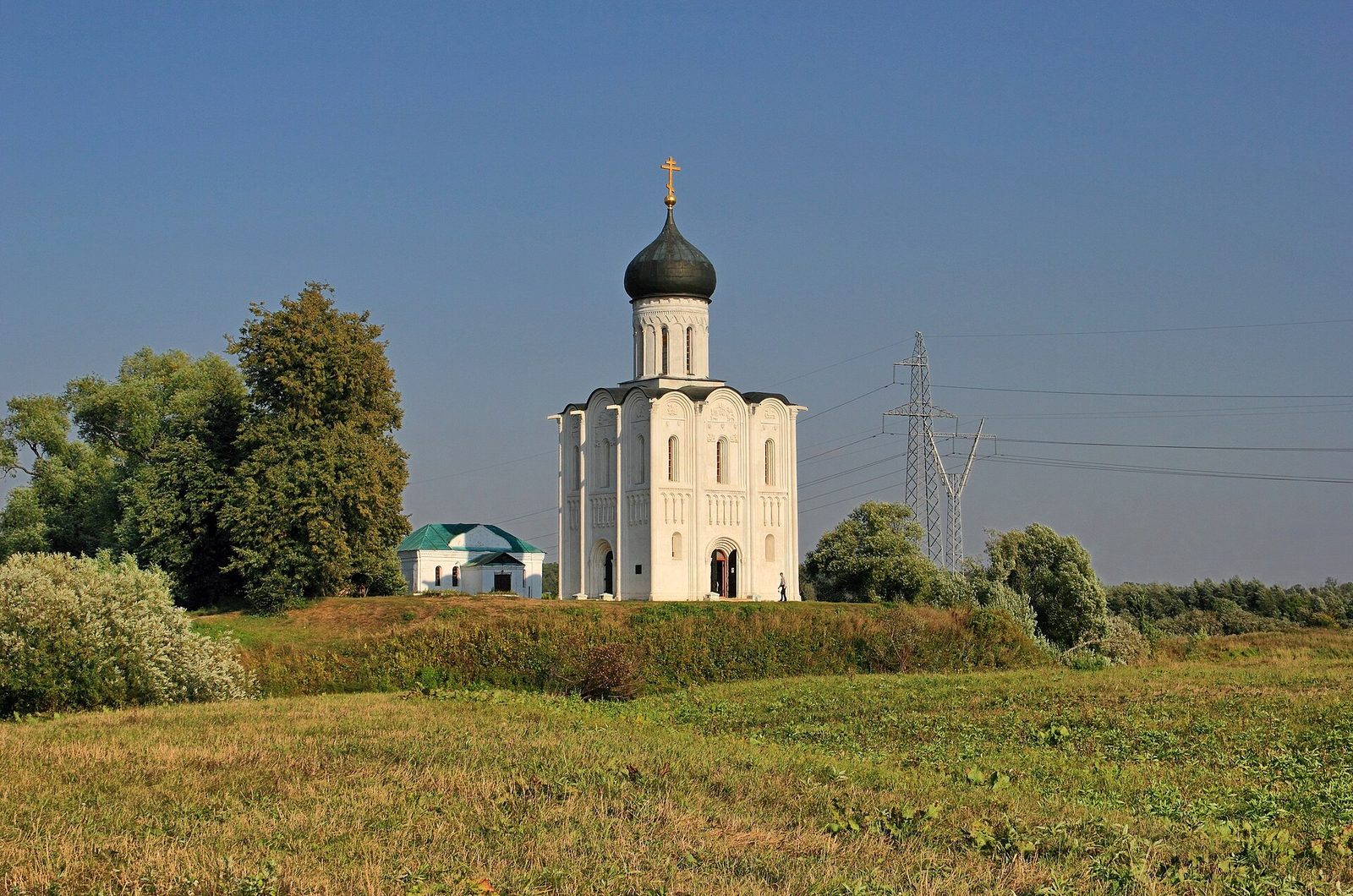 A small white church with a single dome standing alone in a green water-meadow.
