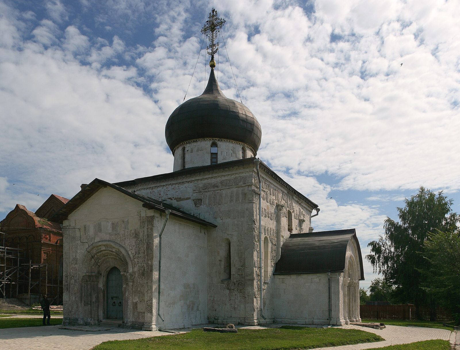 A squat white stone church with a dark onion dome and carved portals.