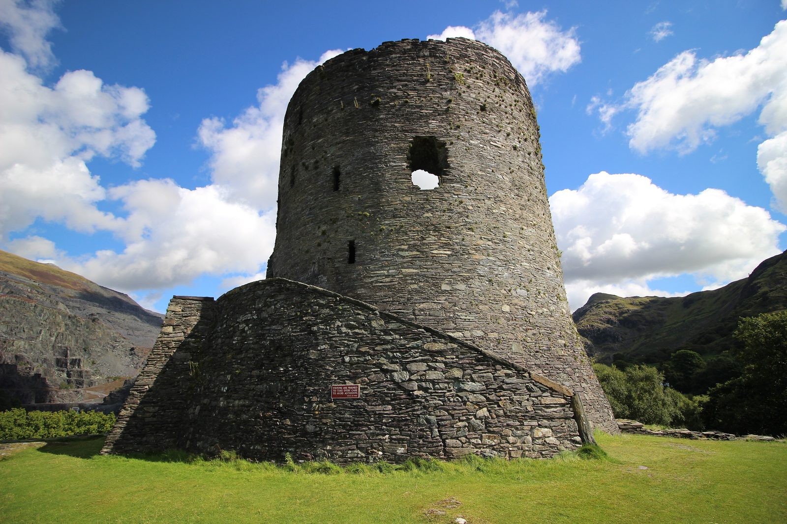 A round stone keep on a grassy mound with mountains behind.