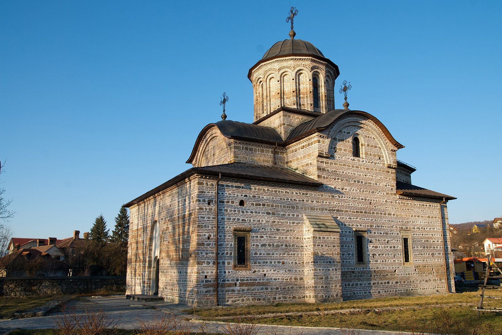 A Byzantine-style church of banded brick and stone with a central dome, against a deep blue sky.