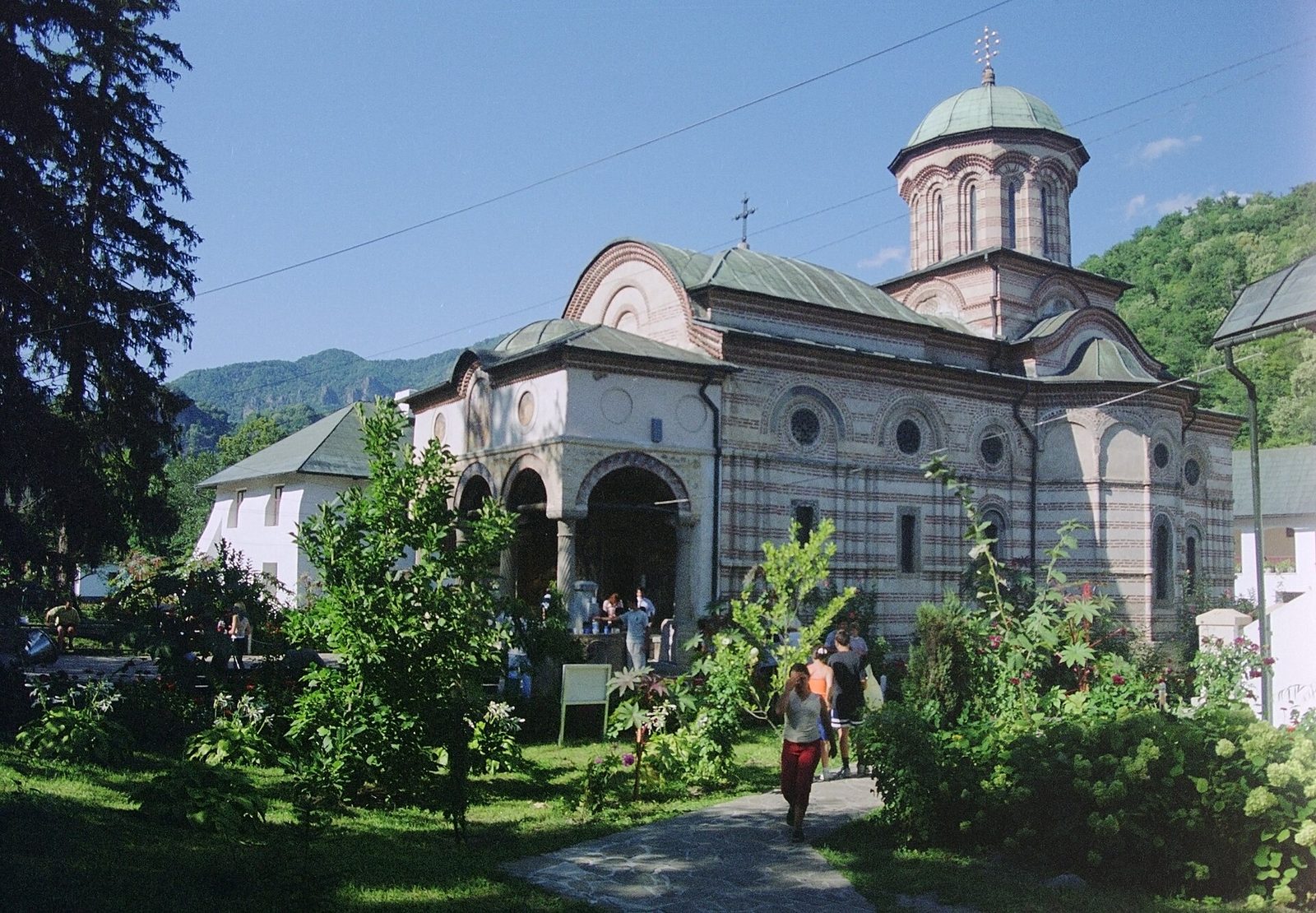 A monastery church with a domed tower and arcaded porch among trees.