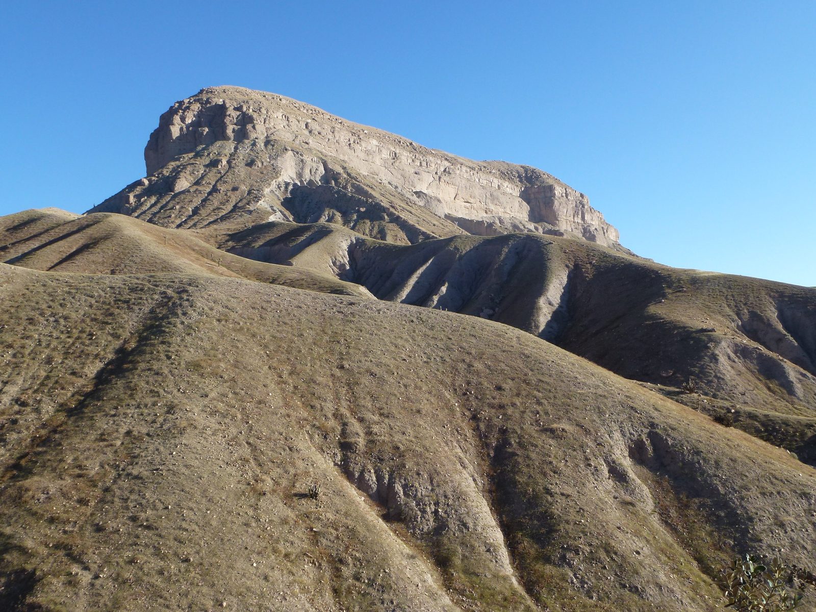 A flat-topped mesa with sheer cliffs rising above bare ridged hills.