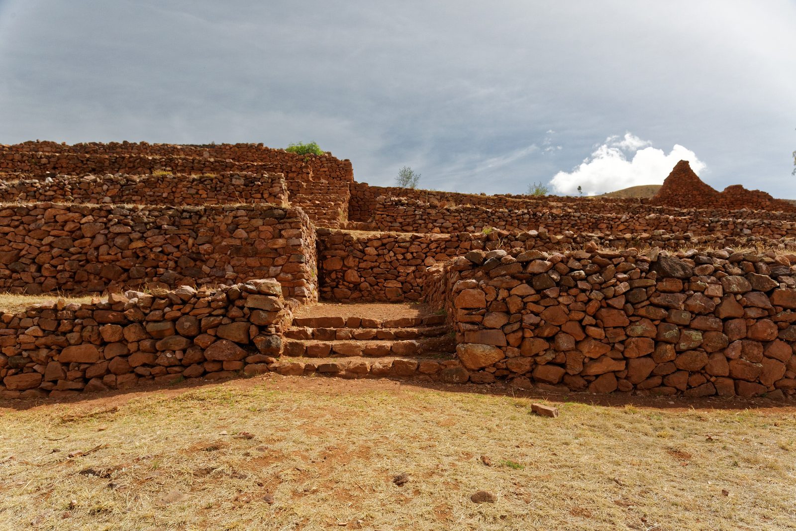 Long walls of rough reddish stone and a short stair inside a ruined enclosure.