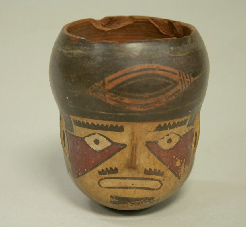 A painted ceramic cup modelled as a human head, with a black hood and red triangles below the eyes.