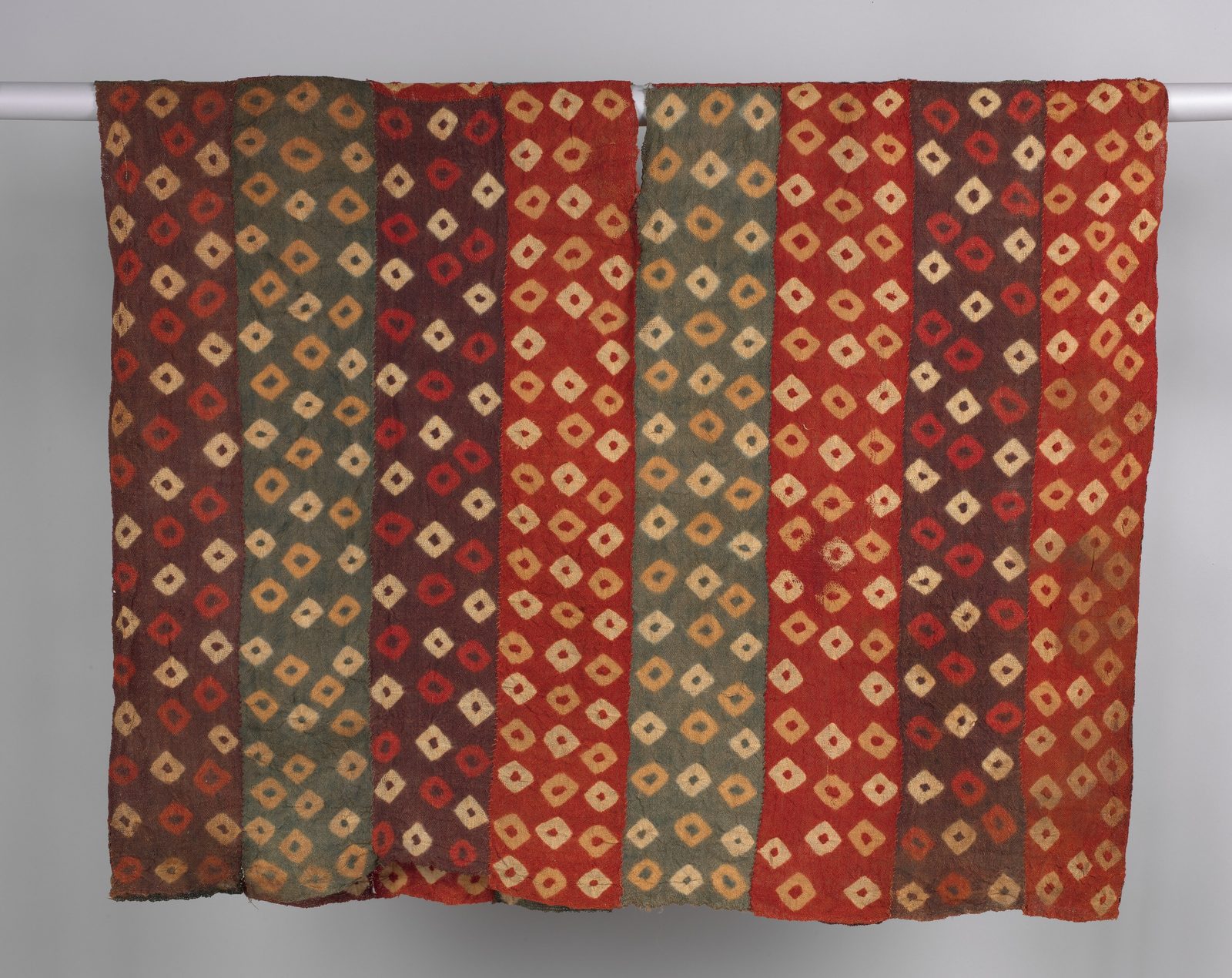 A woven tunic in red, grey and ochre panels covered in small diamond motifs.