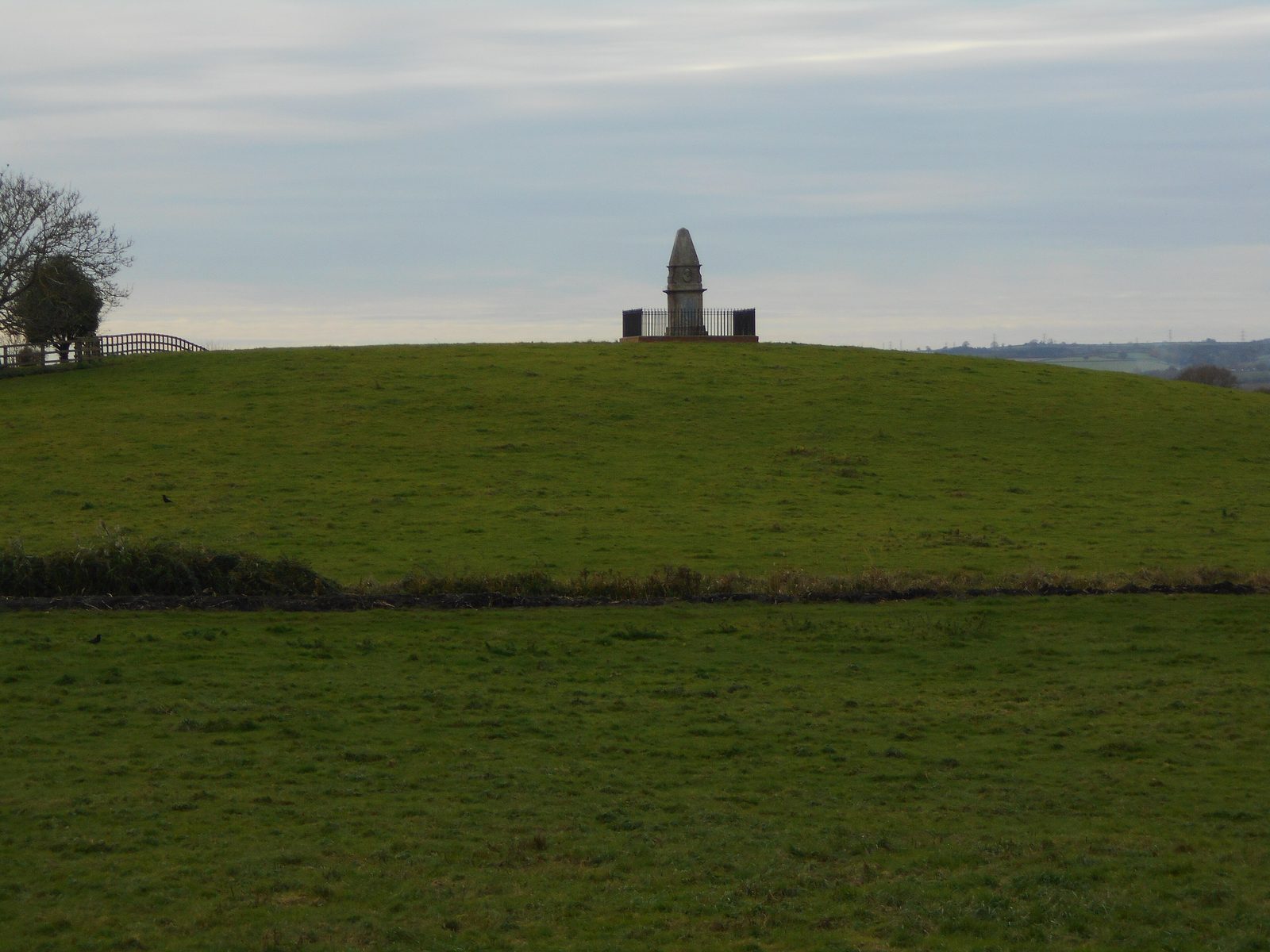 A small stone obelisk on top of a low grassy rise in flat country.