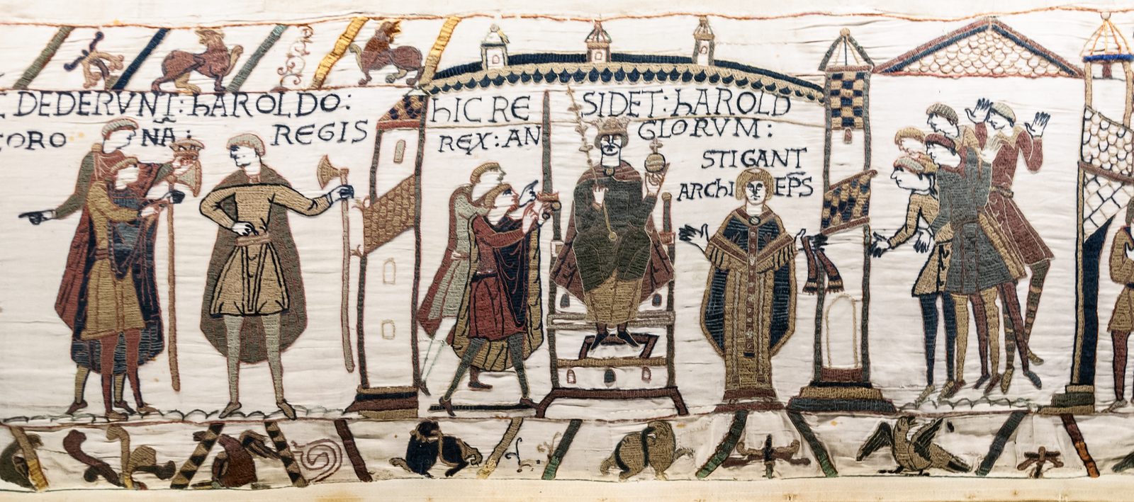 An embroidered strip showing nobles offering a crown, a king enthroned with orb and sceptre, and an archbishop beside him.