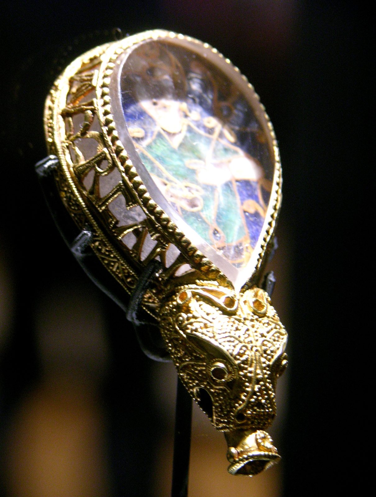 A teardrop-shaped gold ornament enclosing rock crystal over an enamelled figure, ending in an animal head.