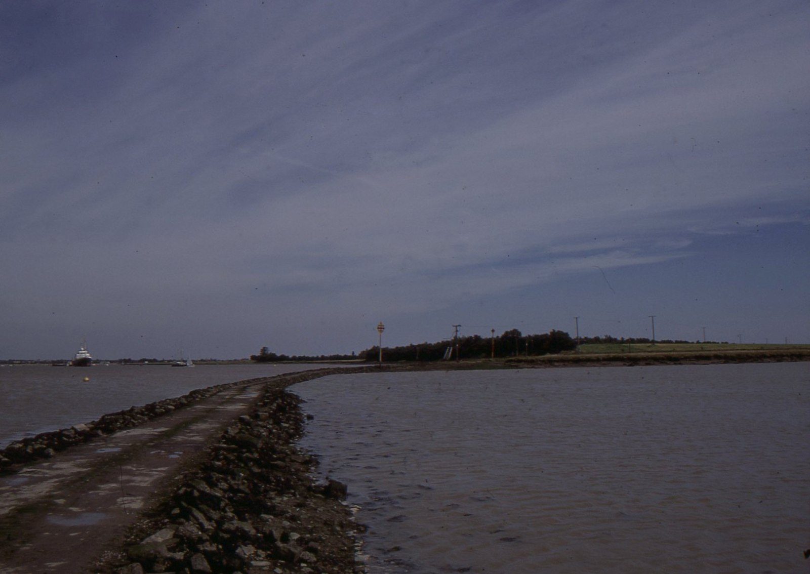 A narrow stone causeway running out across tidal water toward a low island.